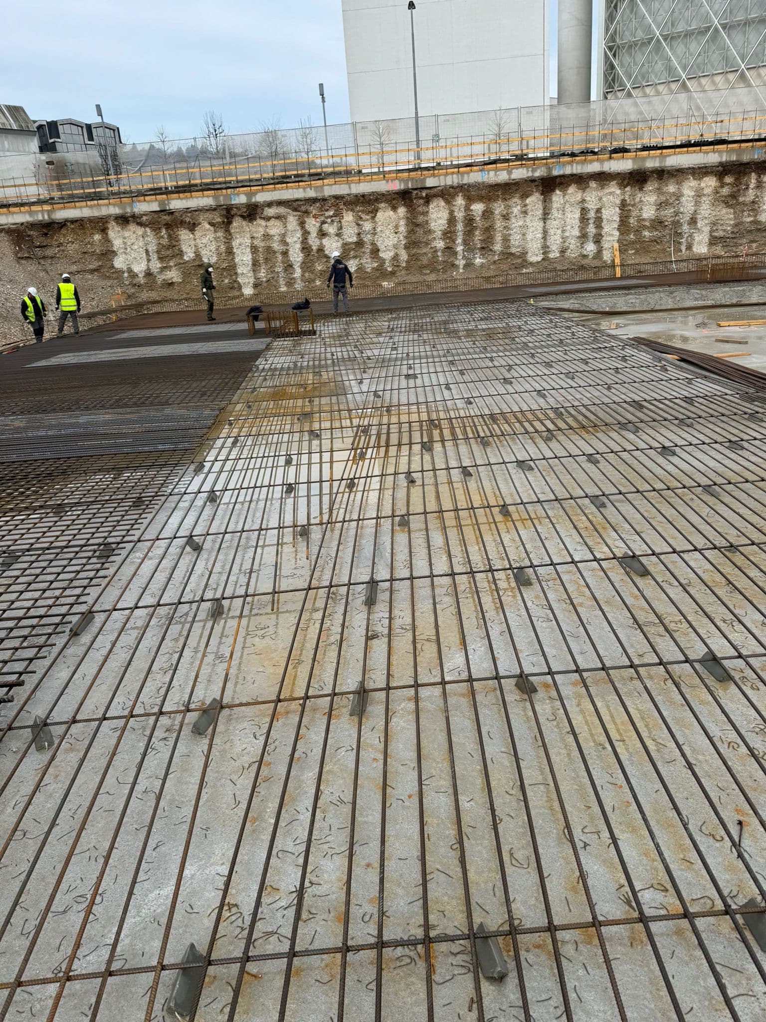 Armaturna mreža za betonsko ploščo z delavci na terenu in varnostnimi ograjami.