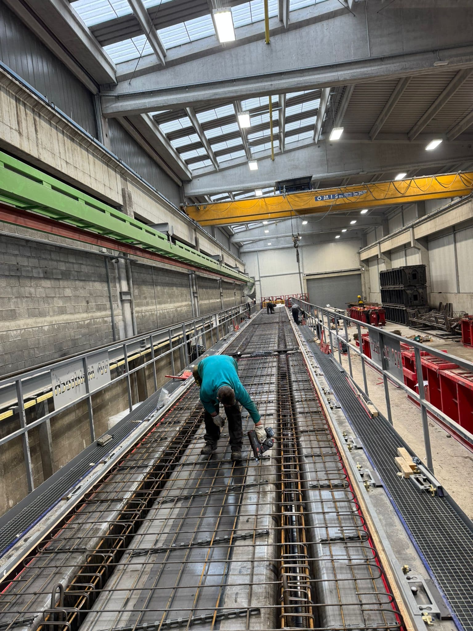 Vgradnja armaturne mreže na dvignjeni poti v veliki industrijski delavnici z mostnim dvigalom.
